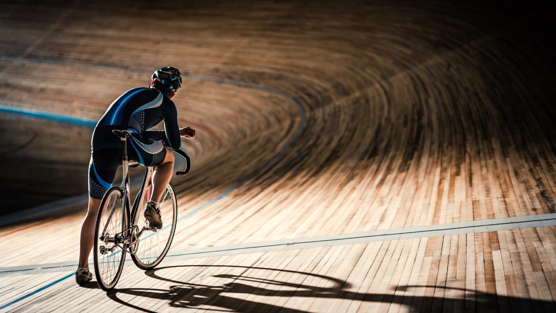 Track cyclist standing with their bike, looking out at a darkened indoor track