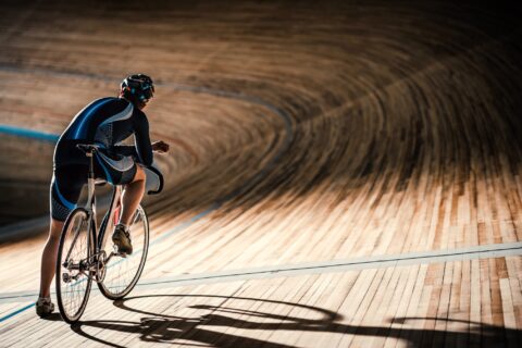 Track cyclist standing with their bike, looking out at a darkened indoor track