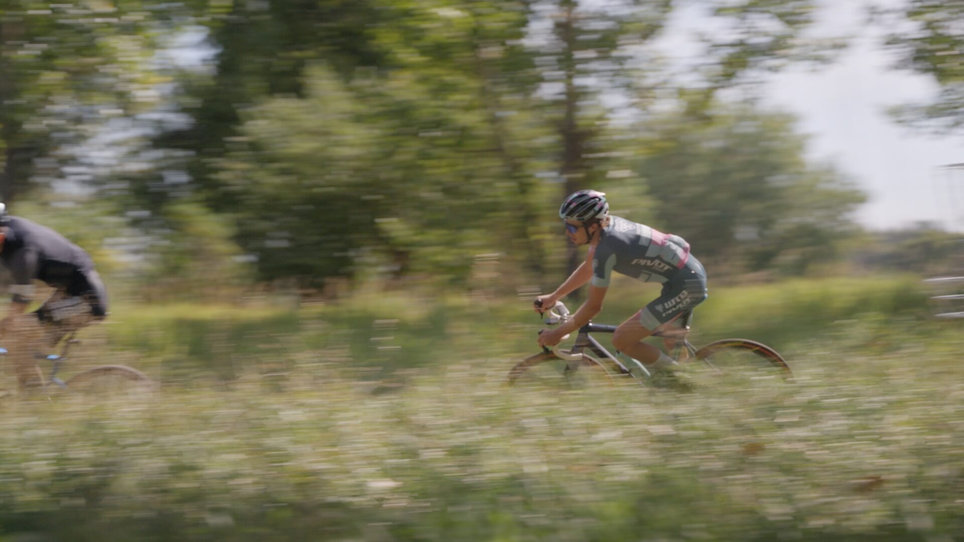 A cyclocross rider rounds a bend through tall grass.