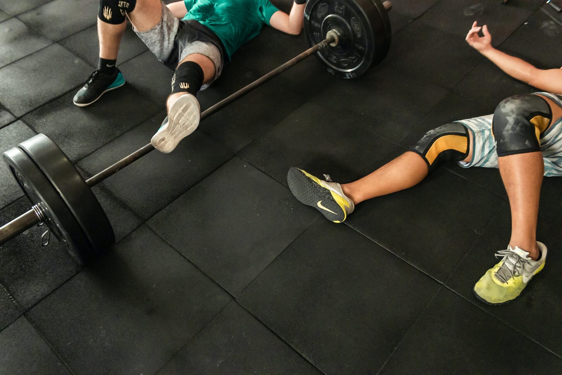 Exhausted athletes laying on a gym floor with a weighted barbell