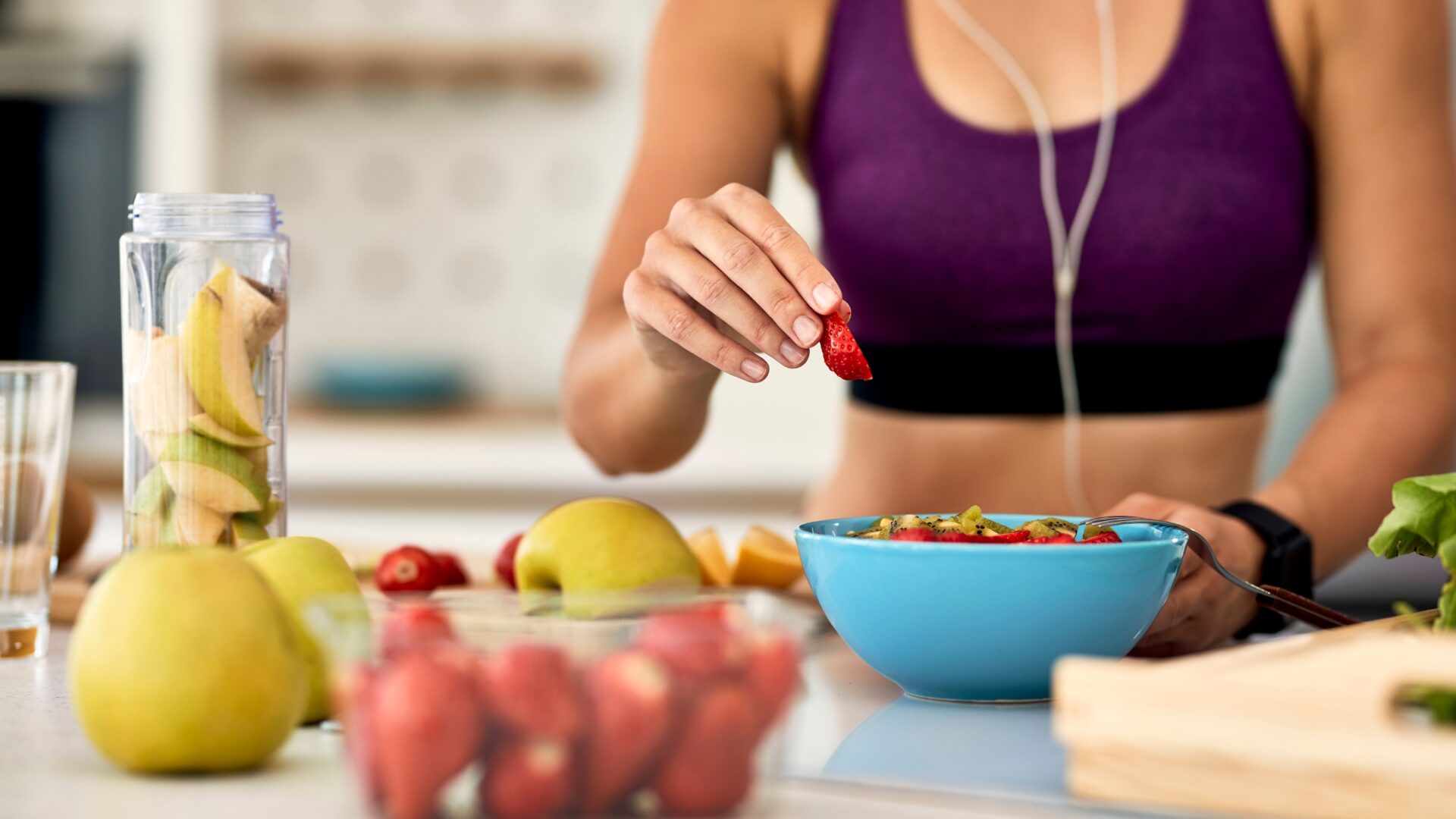 An athletic woman prepares a bowl of fruit.