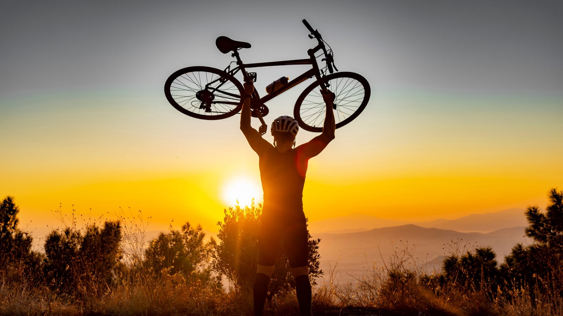 A cyclist celebrates the top of a sunset climb by lifting his bike over his head