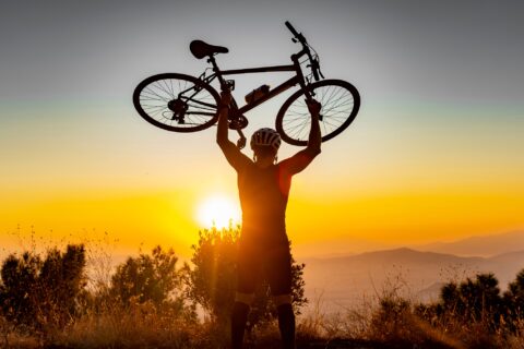 A cyclist celebrates the top of a sunset climb by lifting his bike over his head