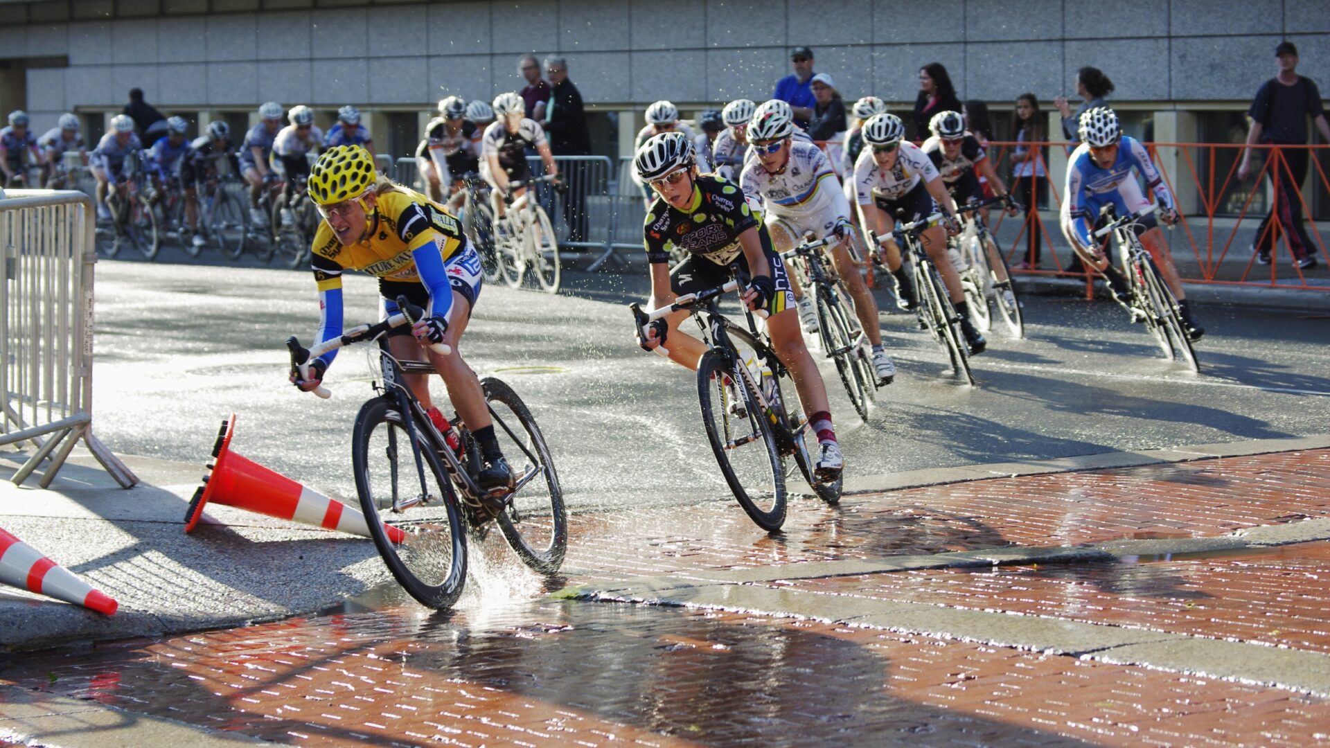 Kristin Armstrong rounds a corner, splashing through standing water as she leads a line of other cyclists