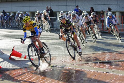 Kristin Armstrong rounds a corner, splashing through standing water as she leads a line of other cyclists