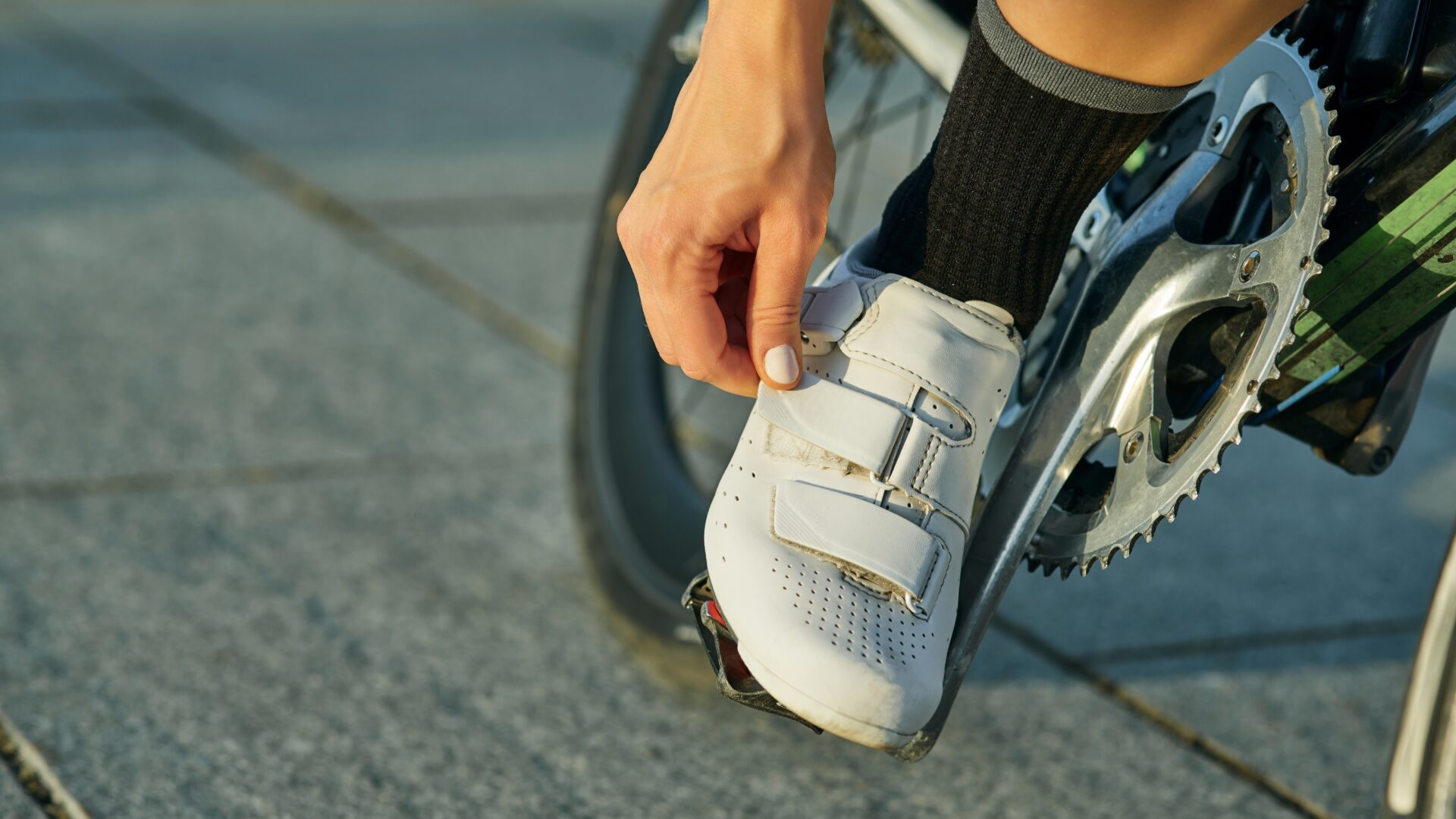 A woman tightens the strap on her white cycling cleat.