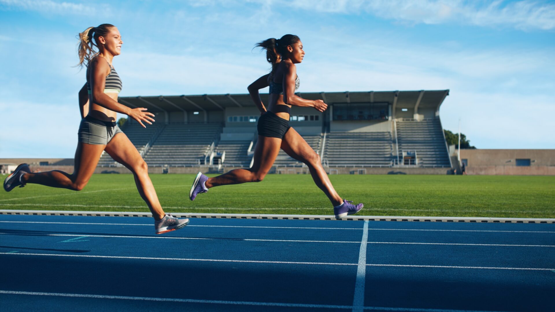 Two women jogging across a blue outdoor running track.