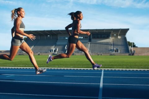 Two women jogging across a blue outdoor running track.