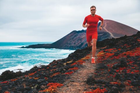 Run race man runner running on mountain trail. Sport athlete ultra running long distance on race competition marathon wearing compression clothes, sunglasses smartwatch wearable device.