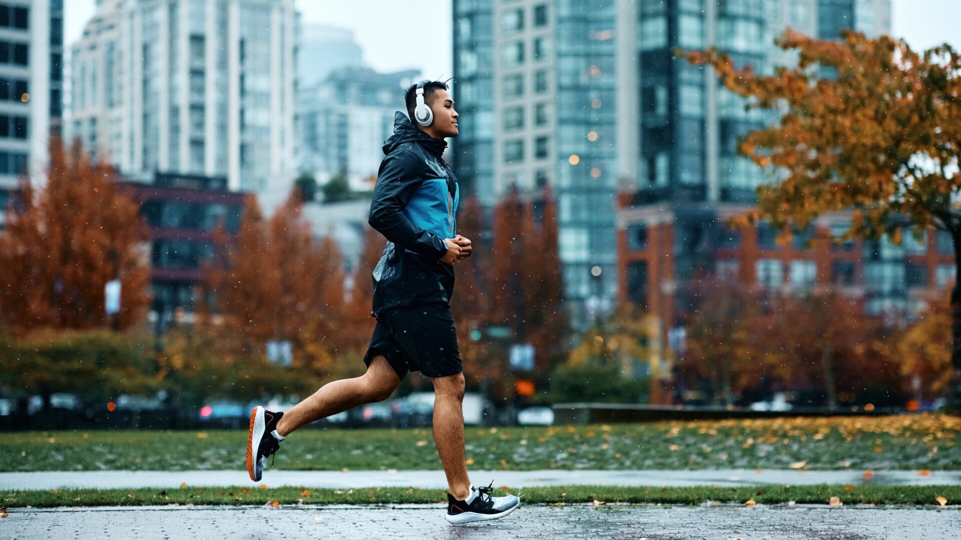 Man wearing headphones jogging through a city on a rainy fall day