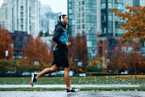 Man wearing headphones jogging through a city on a rainy fall day